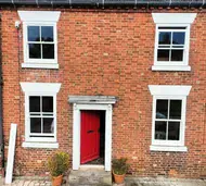 White uPVC vertical sliding sash windows and a red front door on a red-brick terraced house
