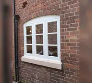 White painted timber casement window with an arched head in an old brick wall
